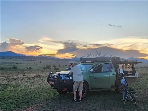 The Toyota Hilux Overland Camping Truck with a tourist looking at the sunset in Kidepo Valley National Park, Uganda.